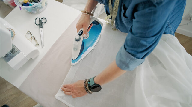 Person ironing white fabric on table in bright workshop