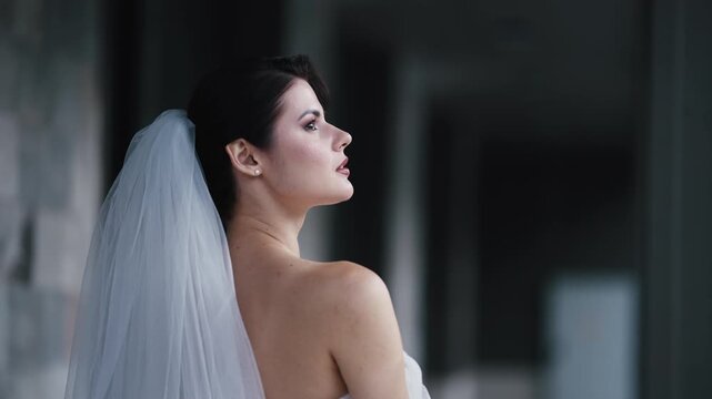 Thoughtful bride in white veil posing in corridor