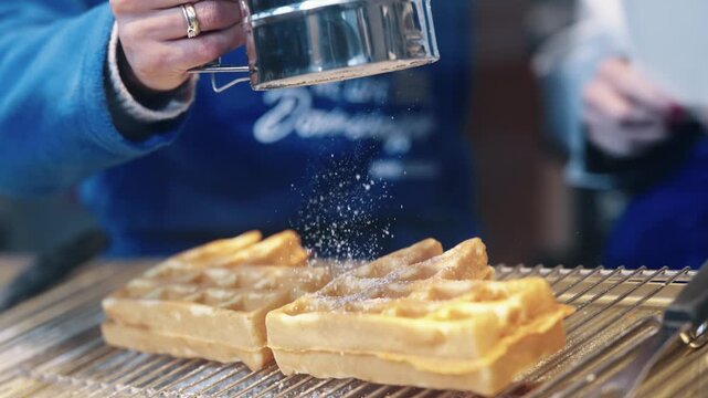 Fresh waffles being sprinkled with powdered sugar at a festive Christmas market in Cologne, slow motion