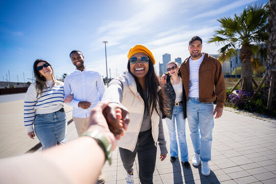 Follow me style travel scene with a cheerful Black woman holding the viewer's hand while friends stand behind in a bright modern neighborhood. Blue sky
