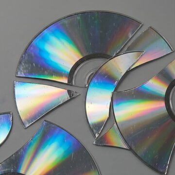 Shattered compact discs scattered on a gray surface, symbolizing data loss and obsolescence of old media.