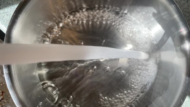 Overhead view of stream of fresh tap water pouring into empty metal pot