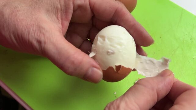 Peel boiled egg. Person hand removes egg white from shell in kitchen during cooking. Woman peeling boiled egg for breakfast. Person is carefully taking out egg white from cracked eggshell in kitchen. 