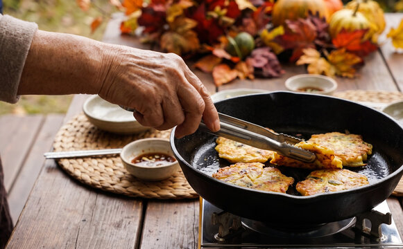 Elderly woman frying traditional Korean mung bean pancakes in a cast iron skillet outdoors in autumn