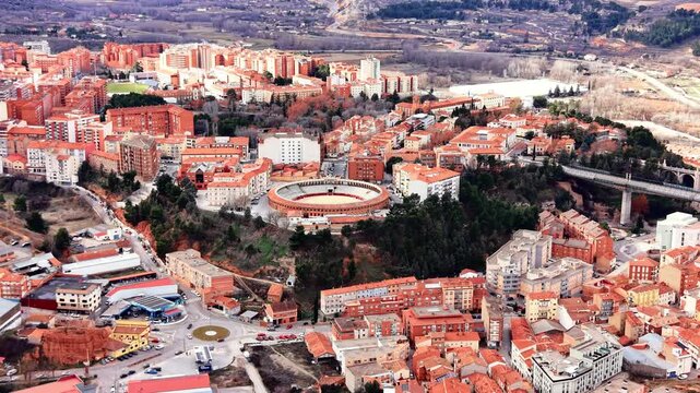 Drone view of Teruel bullring, Spain. Overhead perspective of circular historic arena surrounded by residential neighborhoods and elevated viaduct.