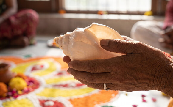 Elderly woman holding a sacred conch shell during a traditional Hindu ritual ceremony