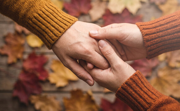 Close up of two people holding hands in autumn with colorful leaves representing love and support