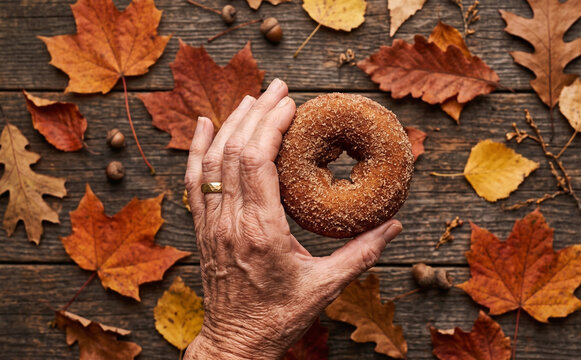Senior woman holding an autumn donut on a rustic wooden background with colorful fall leaves