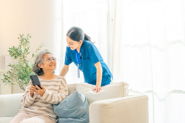 Female caregiver teaching senior woman using smartphone at home, elderly healthcare support with...