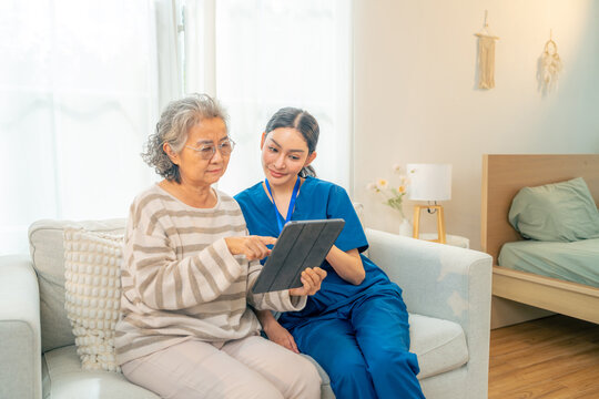 Female caregiver assisting senior woman using digital tablet at home, elderly healthcare support with technology, telemedicine online medical consultation service, aging society and nursing home care.