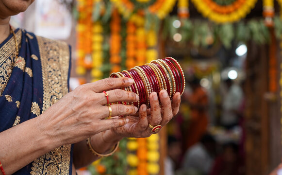 Indian woman holding traditional red and gold bangles during a festive ceremony