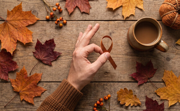 Person holding brown awareness ribbon for uterine cancer or self harm prevention surrounded by autumn leaves and coffee