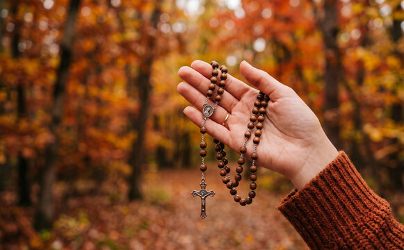 Woman holding wooden rosary beads in autumn forest for prayer and meditation