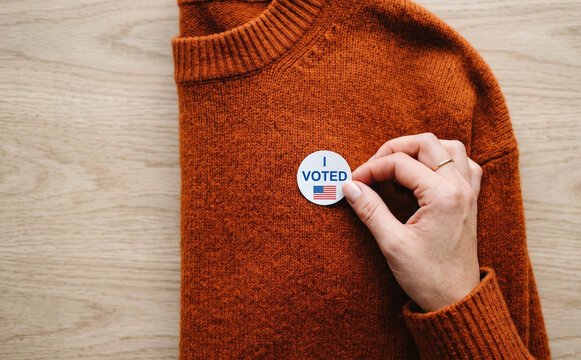 Woman holding an I voted sticker on an orange sweater for election day concept