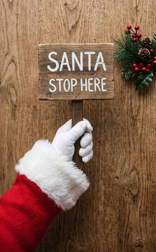 Santa Claus holding a wooden sign that says Santa stop here for Christmas holiday concept