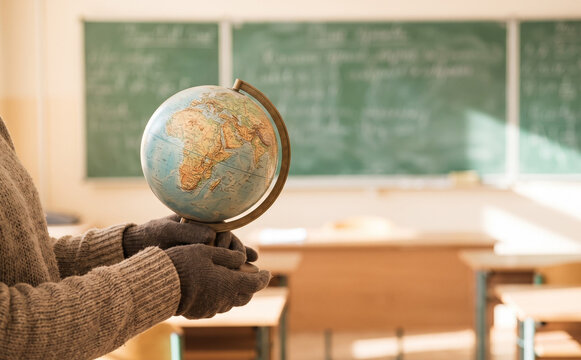 Teacher holding a small globe in a classroom with green chalkboard in background for geography education
