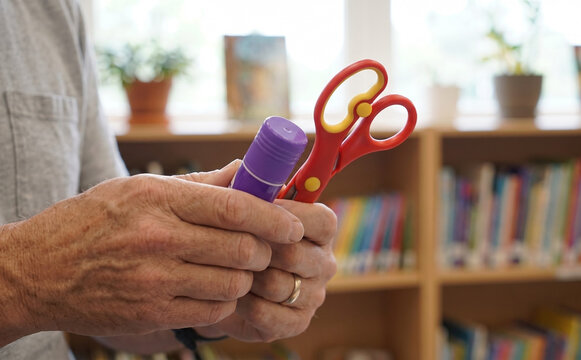 Elderly man holding a glue stick and safety scissors in a classroom setting representing education and crafting