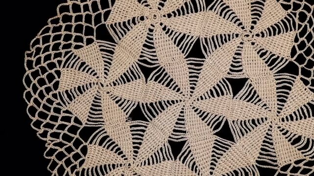 Round crochet beige doily lace isolated on black background, crocheted Grandma's doily, detail of handmade embroidery, tablecloth, napkin, vintage art design. Craft linen. Flat lay, top view, rotating