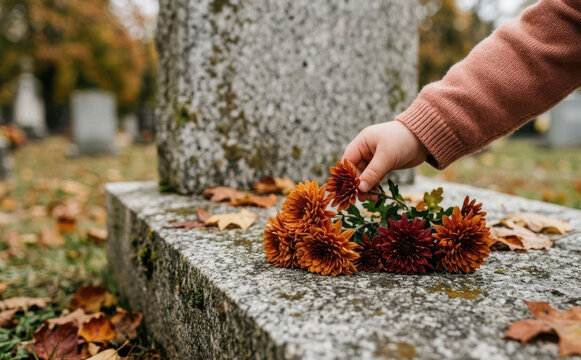 A close-up of a child placing autumn flowers on a grave in a cemetery, representing remembrance and loss
