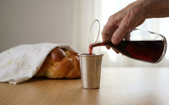 Elderly man pouring red wine into a silver kiddush cup next to a challah bread for Shabbat