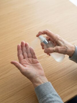 Senior woman disinfecting her hands with an antiseptic spray to protect from viruses and bacteria