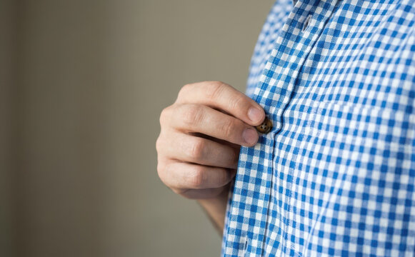 Young adult man buttoning up his blue and white checkered shirt close up concept of getting dressed