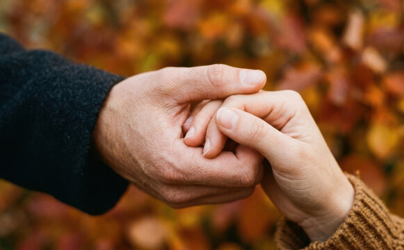 Close-up of adult couple holding hands outdoors in autumn representing love, support, and trust