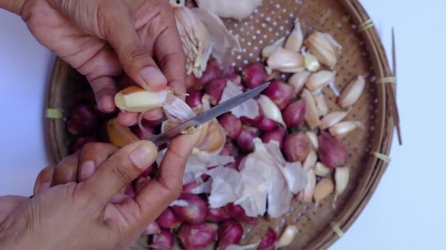 Close up of hands peeling shallots and garlic cloves with knife on a plate, traditional cooking preparation