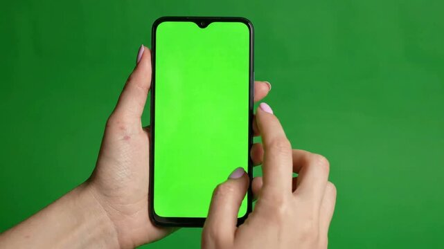 Woman using smartphone with green screen for chroma key compositing, hand holding mobile phone with isolated display for app mockup and digital marketing