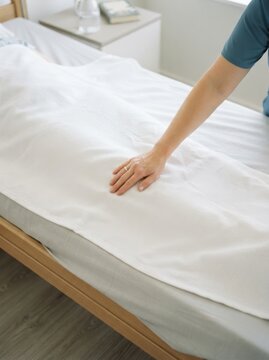 Female nurse tucking in a white blanket on a patient in a hospital bed providing care