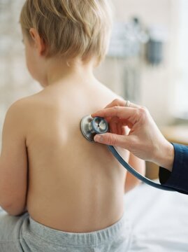 Pediatrician examining toddler boy back with a stethoscope in clinic