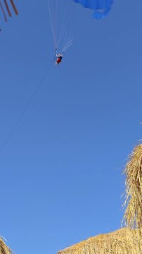 Paraglider soaring above harvested fields under clear blue sky
