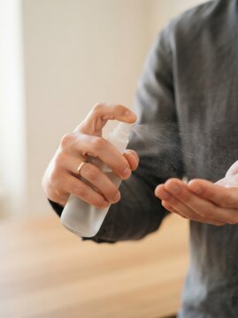 Adult man sanitizing hands with antiseptic spray for hygiene and disease prevention