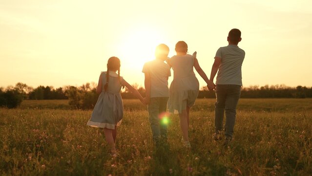 Happy children run towards sunset, girl boy holding hands run play, fun summer holidays, children recreation, childhood wonder moments, learning cooperation skills, sunset meadow walk, peaceful