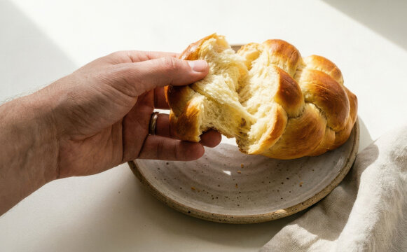 Close up of male hands pulling apart freshly baked homemade braided challah bread on ceramic plate