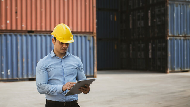 Asian Male Construction Worker in Yellow Safety Helmet Using Tablet at Shipping Container Yard
