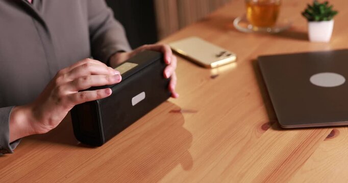 Woman using modern audio speaker at wooden table, closeup