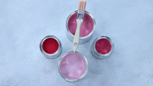 Cans with paint in shades of pink and brush on light grey table, flat lay