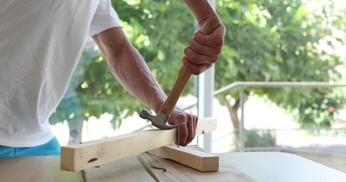 Man pulling metal nail out of wooden plank at table indoors, closeup