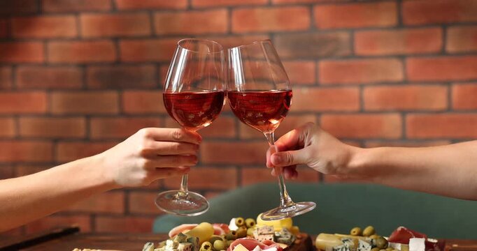 Friends clinking glasses of wine at table indoors, closeup