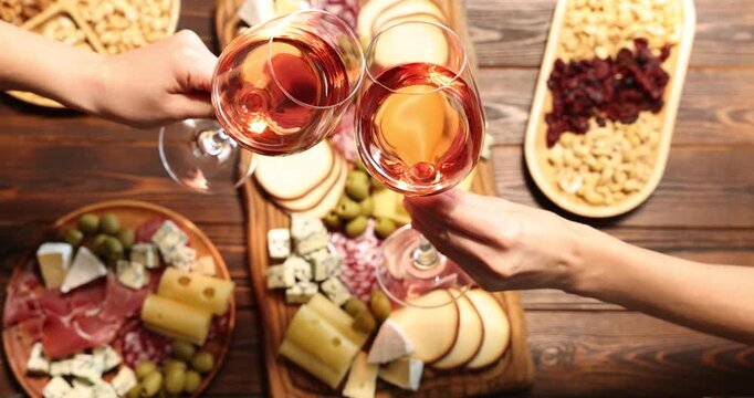 Friends clinking glasses of wine at wooden table indoors, top view