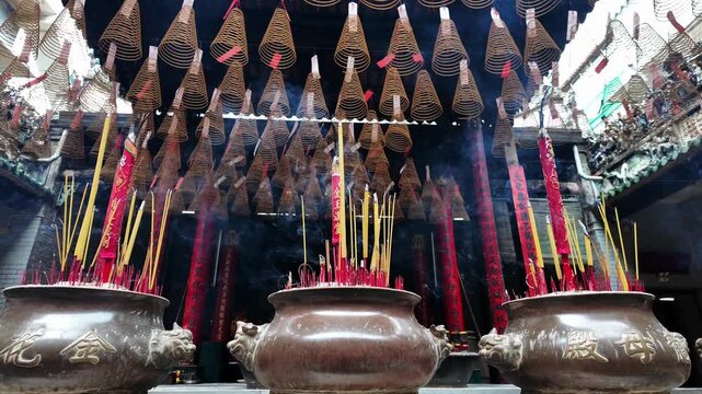 Smoke rising from traditional incense sticks in an ornate burner surrounded by hanging spiral incense coils in a historic Chinese temple, Cholon, District 5, Ho Chi Minh City, Vietnam