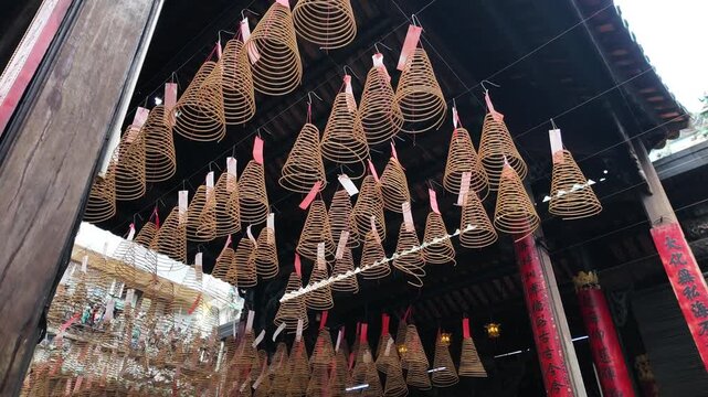 Smoke rising from traditional incense sticks in an ornate burner surrounded by hanging spiral incense coils in a historic Chinese temple, Cholon, District 5, Ho Chi Minh City, Vietnam