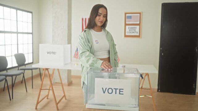 Woman places ballot into clear ballot box, hand over slot, inside a polling building; civic participation pride.