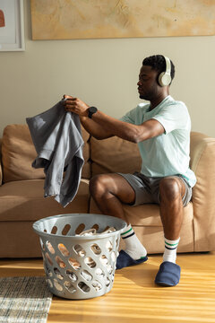 Man sitting on sofa in living room, folding sweatshirt into laundry basket, copy space