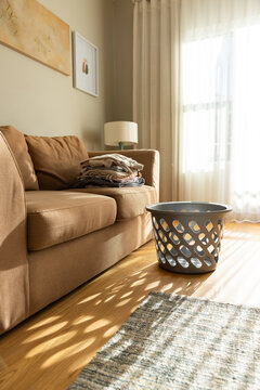 Brown upholstered sofa is sitting in sunlit living room with folded laundry and lattice basket