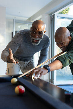 African American men playing pool at home, shooter wearing dark green top lining up with cue