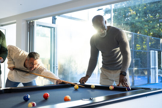 African American men leaning over blue-felt pool table in residential rec room, aiming cues