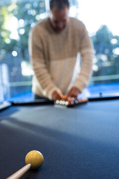 Adult man in sweater leaning on blue-felt pool table racking at home with cue ball, cue-stick