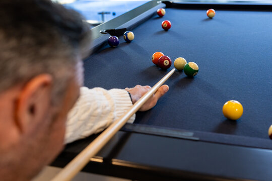 Man wearing knit sweater leaning over blue-felt table in pool hall, aiming cue at billiard balls